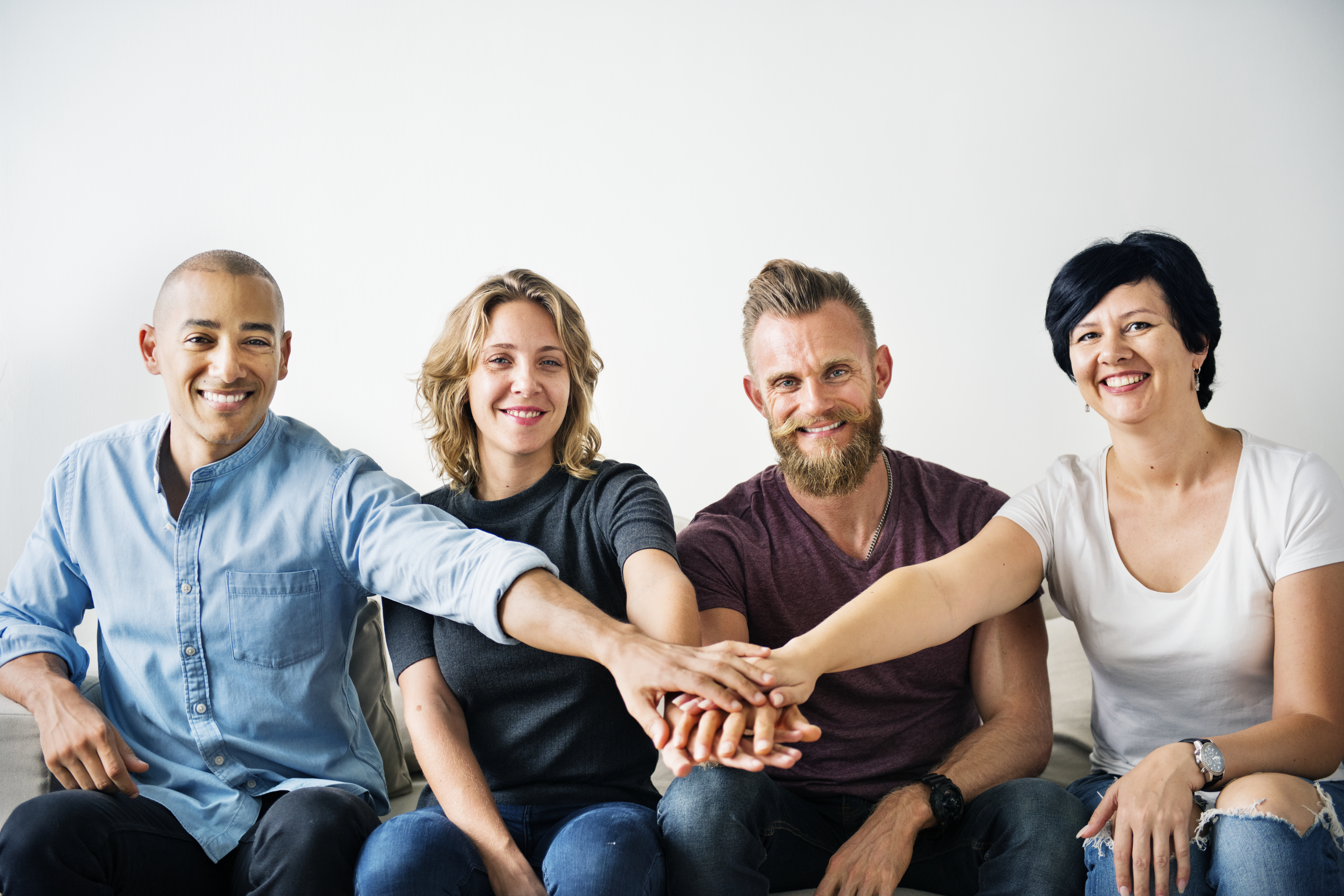 4 people sitting in a line and smilling. They have each put one hand in to a pile of 4 hands together.